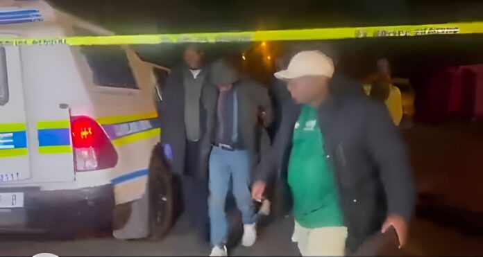 South African police officers escort murder suspect Ndodana Tshuma following his arrest in Johannesburg linked to the Bedfordshire family deaths. South African police officers escort murder suspect Ndodana Tshuma following his arrest in Johannesburg linked to the Bedfordshire family deaths.